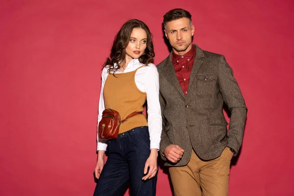 Belo casal na moda em desgaste formal posando no fundo vermelho com espaço de cópia — Fotografia de Stock