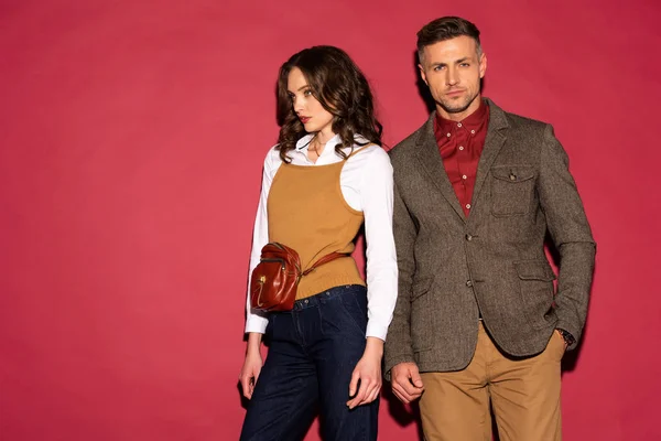 Beautiful fashionable couple in formal wear posing on red background with copy space — Stock Photo