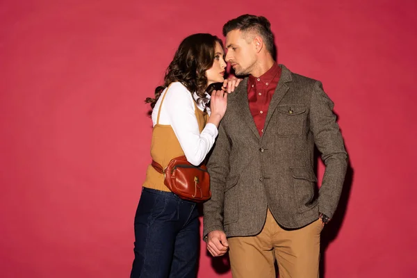 Beautiful woman in formal wear embracing handsome man on red background — Stock Photo