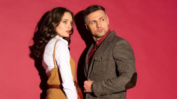 Beautiful fashionable couple in formal wear looking away while posing on red background — Stock Photo