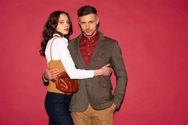 Hermosa pareja de moda en ropa formal abrazando y posando sobre fondo rojo - foto de stock
