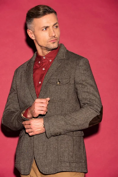 Handsome man in formal wear looking away while adjusting jacket on red background — Stock Photo