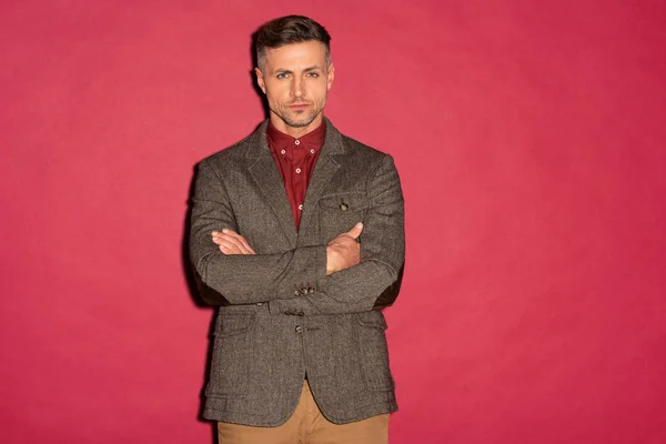 Handsome stylish man in formal wear with arms crossed looking at camera on red background — Stock Photo