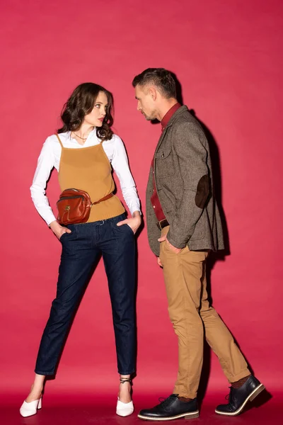 Красивая стильная пара в формальной одежде позируют и смотрят друг на друга на красном фоне — стоковое фото