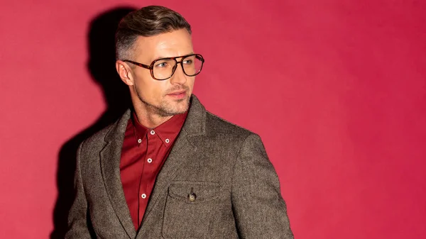 Hombre con estilo de confianza en el desgaste formal y gafas mirando hacia otro lado sobre fondo rojo - foto de stock