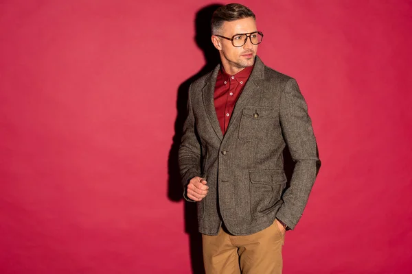Впевнений стильний чоловік у формальному одязі та окулярах на червоному тлі з копіювальним простором — стокове фото