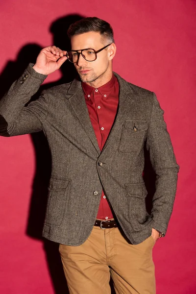 Hombre con estilo de confianza en el desgaste formal y gafas mirando hacia otro lado sobre fondo rojo - foto de stock