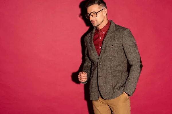 Uomo elegante fiducioso in abbigliamento formale e occhiali su sfondo rosso con spazio copia — Foto stock