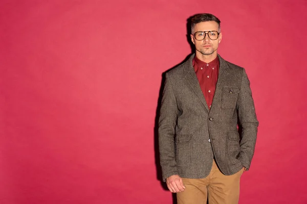 Stylischer Mann mit Brille und formaler Kleidung, der in die Kamera auf rotem Hintergrund mit Kopierraum blickt — Stockfoto