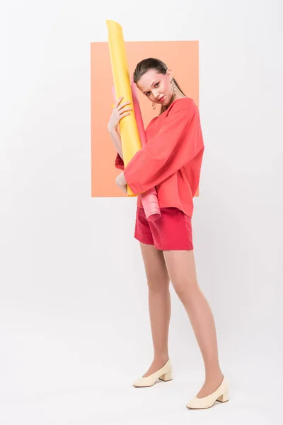 Hermosa chica de moda sosteniendo rollos de papel, mirando a la cámara y posando con coral vivo en el fondo - foto de stock
