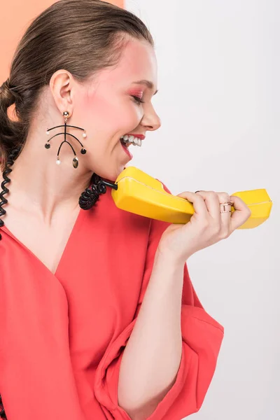 Stylish girl on living coral clothes shouting at retro telephone on white background — Stock Photo