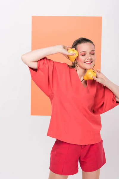 Hermosa sonriente chica de moda sosteniendo peras y posando con coral vivo en el fondo - foto de stock