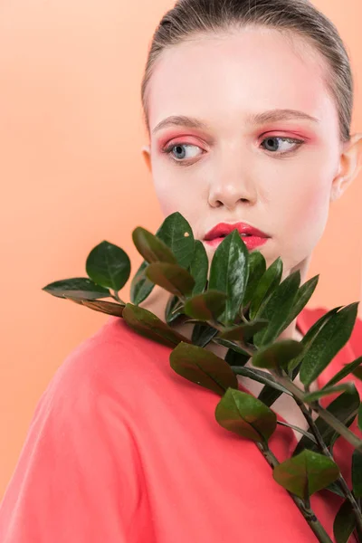 Beautiful stylish girl looking away and posing with plant isolated on living coral — Stock Photo