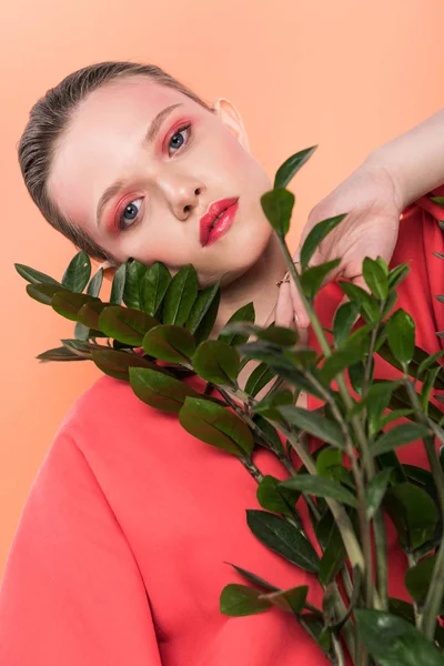 Beautiful stylish girl looking at camera and posing with plant isolated on living coral — Stock Photo