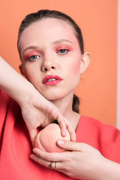 Beautiful fashionable girl holding peach, looking at camera and posing with living coral on background — Stock Photo