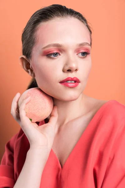 Fashionable girl holding peach and posing with living coral on background — Stock Photo