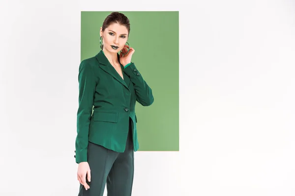 Hermosa mujer de moda en ropa formal tocando la cara y posando con verde marino en el fondo - foto de stock