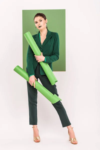 Beautiful stylish woman holding paper rolls, looking at camera and posing with sea green on background — Stock Photo
