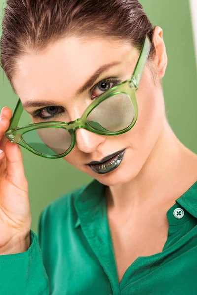 Портрет красивой модной женщины в солнечных очках, смотрящей в камеру с зеленым на заднем плане — стоковое фото