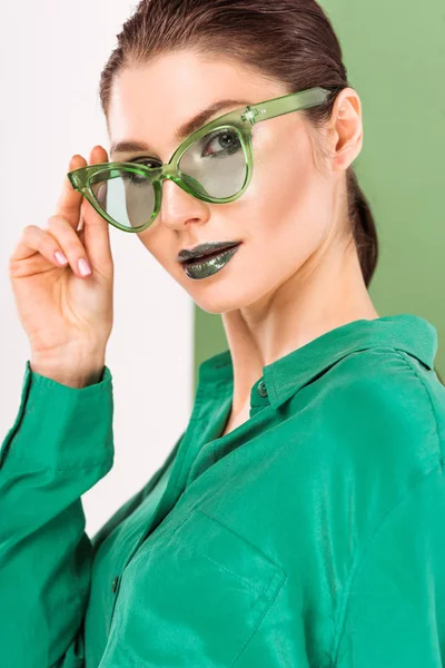 Beautiful fashionable woman in sunglasses posing and looking at camera with sea green on background — Stock Photo
