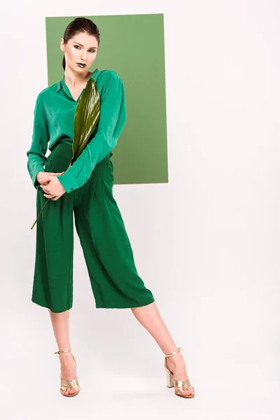 Hermosa mujer con estilo mirando a la cámara, sosteniendo la hoja y posando con verde marino en el fondo - foto de stock