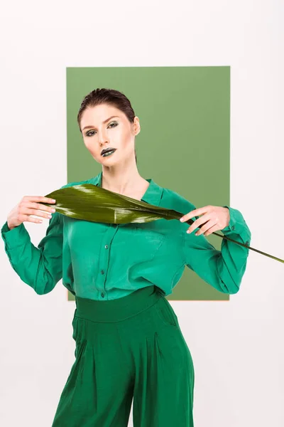 Hermosa mujer con estilo mirando a la cámara, sosteniendo la hoja y posando con verde marino en el fondo — Stock Photo