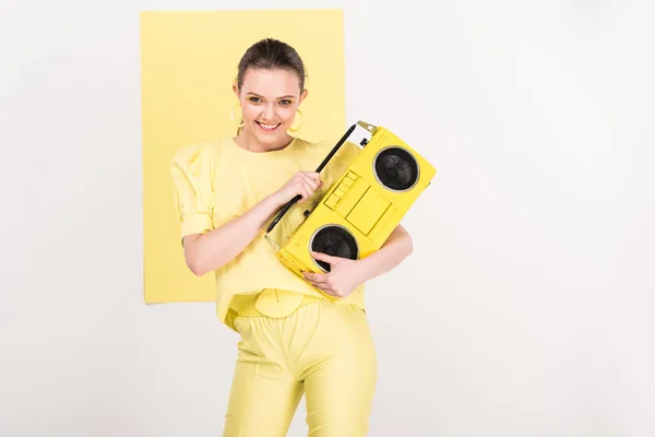 Stylish smiling girl holding retro boombox, looking at camera and posing with limelight on background — Stock Photo