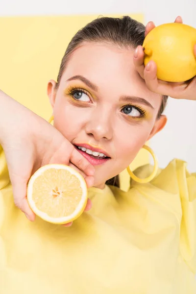 Bela menina elegante segurando limões, sorrindo e posando com holofotes no fundo — Fotografia de Stock