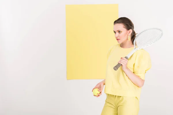 Beautiful stylish girl holding tennis racket and ball while posing with copy space and limelight on background — Stock Photo