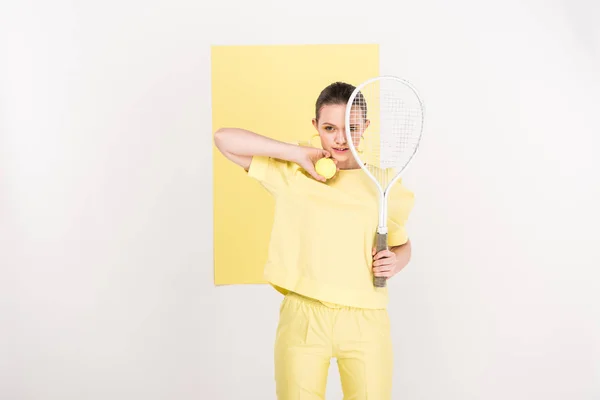 Hermosa chica elegante sosteniendo raqueta de tenis y pelota mientras posa con espacio de copia y centro de atención en el fondo - foto de stock