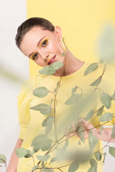 Selective focus of attractive stylish girl holding plant and posing with limelight on background — Stock Photo