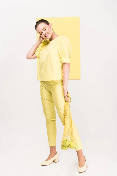 Attractive stylish girl holding string bag with apples while posing with limelight on background — Stock Photo