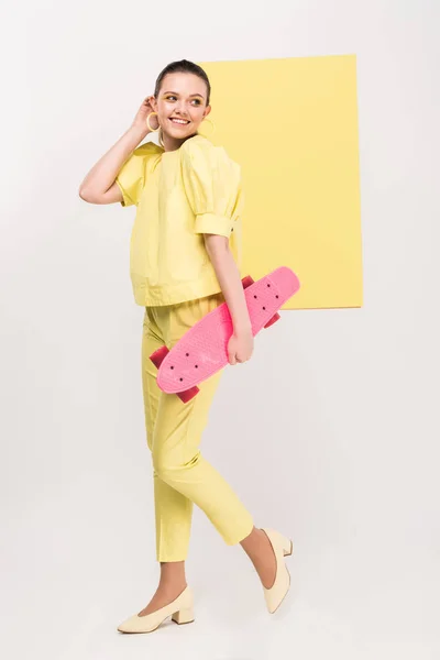 Beautiful stylish girl holding skateboard and posing with limelight on background — Stock Photo