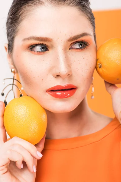 Bela mulher elegante segurando laranjas, olhando para longe e posando com açafrão no fundo — Fotografia de Stock