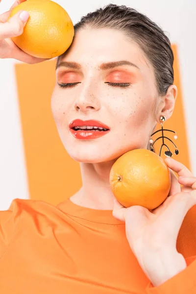 Belle femme élégante avec les yeux fermés tenant des oranges et posant avec curcuma sur fond — Photo de stock