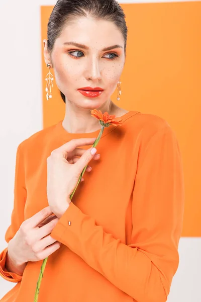 Hermosa mujer joven sosteniendo la flor, mirando hacia otro lado y posando con cúrcuma en el fondo — Stock Photo