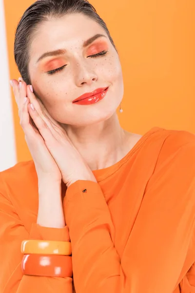 Hermosa mujer de moda con los ojos cerrados, apoyando la cabeza en las manos y posando con cúrcuma en el fondo — Stock Photo