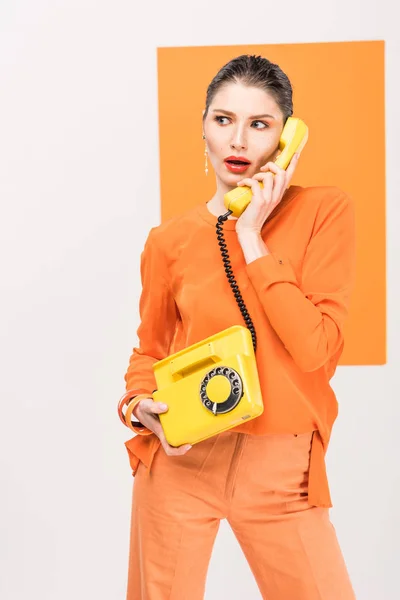 Surprised fashionable young woman talking on retro telephone and posing with turmeric on background — Stock Photo