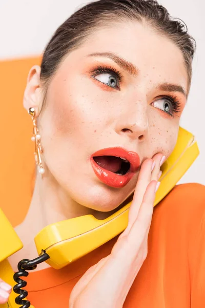 Beautiful surprised woman talking on retro telephone and touching face with turmeric on background — Stock Photo