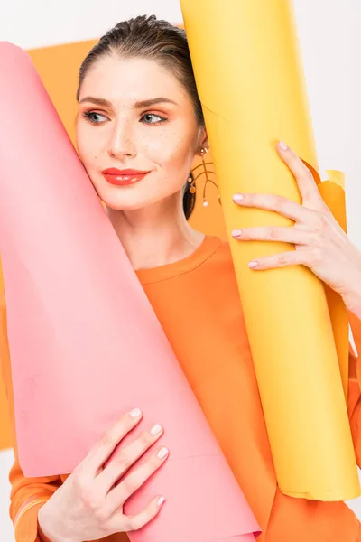 Enfoque selectivo de la mujer joven con estilo en ropa cúrcuma sonriendo y posando mientras sostiene rollos de papel - foto de stock