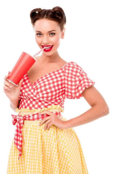Smiling pin up girl drinking from paper cup with straw isolated on white — Stock Photo