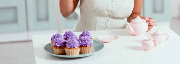 Vue recadrée de la femme assise à table avec assiette de cupcakes — Photo de stock
