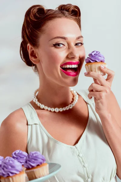 Sonriendo pin up chica va a degustar cupcake casero con crema púrpura - foto de stock