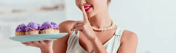 Cropped view of pretty pin up girl holding plate of cupcakes and showing shh sign — Stock Photo