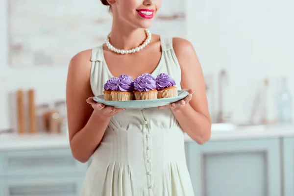 Partial view of pin up gilr holding plate of cupcakes — Stock Photo