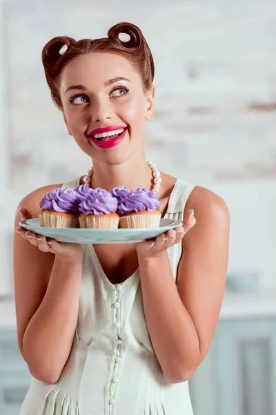 Delighted smiling pin up gilr holding plate of cupcakes — Stock Photo