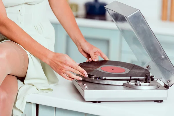 Cropped view of pin up girl sitting on table with crossed legs and putting vinyl record on record player — Stock Photo