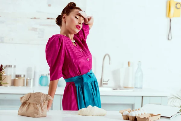 Exhausted pin up girl with flour traces on hands and face resting by kitchen table — Stock Photo
