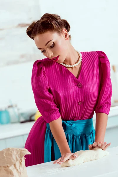 Attractive pin up girl in crimson dress and blue apron kneading dough — Stock Photo