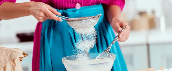 Cropped view of woman girl in blue apron sifting flour — Stock Photo
